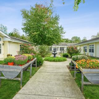 A charming garden courtyard with a central pathway flanked by lush greenery and vibrant flowers.