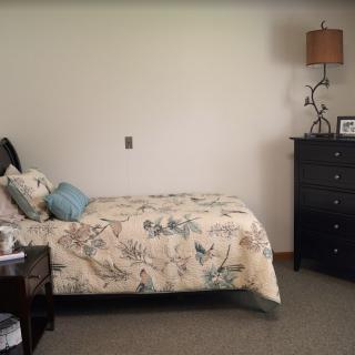 A cozy bedroom with a floral-patterned bedspread, dark wooden dresser, and lamp.