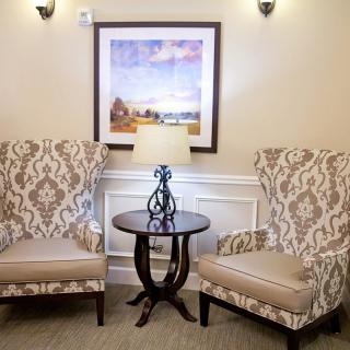 A cozy sitting area with two patterned chairs and a small round table featuring a decorative lamp, set against a wall with framed artwork.