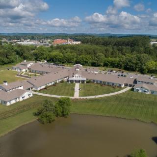 Aerial view of a campus with a central building surrounded by greenery and a pond.