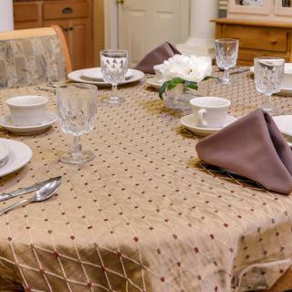 An elegantly set dining table with a patterned tablecloth, complete with dinnerware, glasses, and folded napkins.