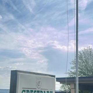 A sign with a partly cloudy sky in the background, next to a building and a tree.