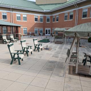A spacious courtyard with green outdoor seating and sunshades, surrounded by a brick building.