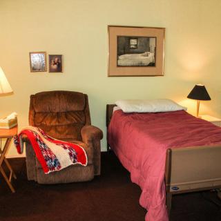 A cozy bedroom setup with a bed next to an armchair and lamps providing warm lighting.