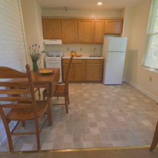 A cozy kitchen and dining area featuring wooden cabinets, a small table with chairs, a refrigerator, and a stove.