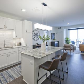 A modern open-plan kitchen with a central island and bar stools, leading into a cozy living and dining area.