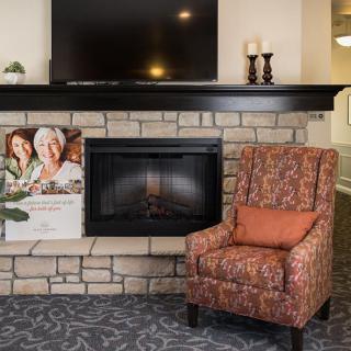 A cozy living room setup featuring a stone fireplace, television, patterned armchair, and decorative candles.