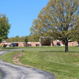 A scenic view of a building surrounded by trees and grass, with a road leading up to it under a clear blue sky.