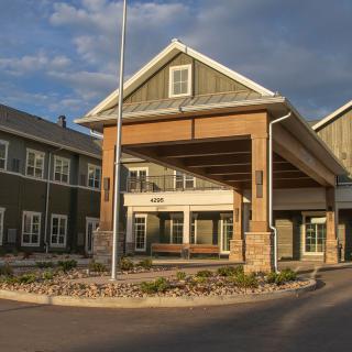 A modern building with a covered entrance and well-maintained surroundings under a clear sky.
