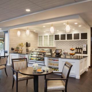 A modern cafe interior featuring a seating area with tables and chairs, a counter with a display case, and stylish lighting.