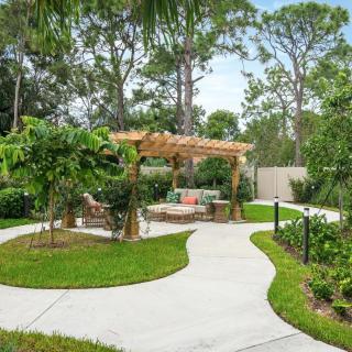 A tranquil garden setting with a wooden pergola and a winding concrete pathway surrounded by lush greenery.