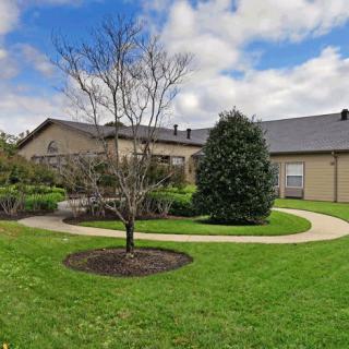 A residential house with a well-maintained lawn, a tree, and a curving walkway under a partly cloudy sky.