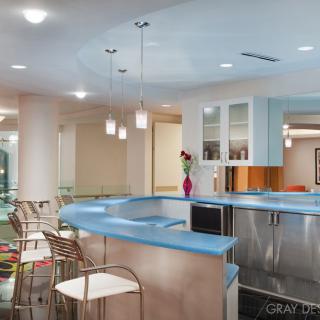 A modern kitchen with a blue countertop and pendant lighting, featuring bar stools and an open design.