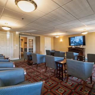 A comfortable lounge area with multiple chairs facing a television, featuring warm lighting and a patterned carpet.