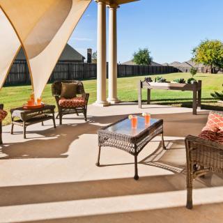 A sunny patio with stylish outdoor furniture and a shade sail overlooking a spacious backyard.
