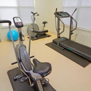 A small gym with various exercise equipment, including a treadmill, stationary bike, and elliptical machine.