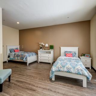 A cozy bedroom featuring two twin beds with patterned bedspreads, a dresser in between, and warm wood flooring.