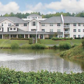 A scenic view of a large building by a tranquil lake surrounded by greenery.
