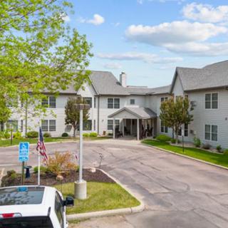 A residential building with a parking lot and trees under a partly cloudy sky.