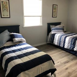A bedroom with two twin beds featuring striped bedding, a window in between, and framed pictures on the wall.