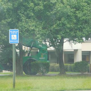 A green landscaping vehicle parked near a designated parking spot, surrounded by trees and grass.