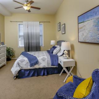 A cozy bedroom with blue and white decor, featuring a bed, dresser, lamps, and wall artwork.
