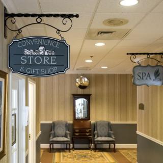 A hallway with signs pointing to a convenience store and spa, featuring a seating area with chairs and a decorative clock.