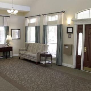 A cozy lobby area with a sofa, table, and lamp by large windows adorned with curtains.
