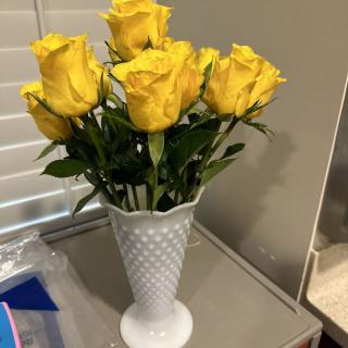 A bouquet of vibrant yellow roses in a white vase, elegantly placed on a table.