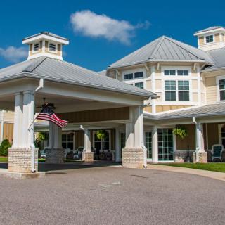 A large residential building with a covered entrance and an American flag, set against a clear blue sky.