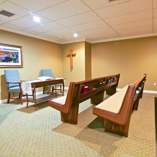 A small chapel interior with pews, an altar, and a cross on the wall.