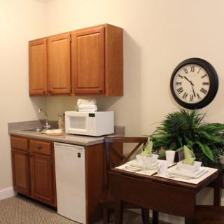 A kitchenette featuring wooden cabinets, a microwave, a sink, and a decorative clock on the wall.