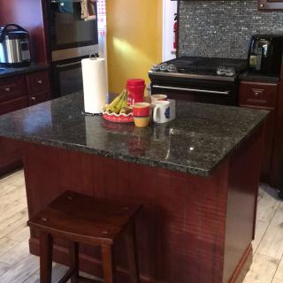 A kitchen featuring a central island with a granite countertop, surrounded by wooden cabinets and appliances.