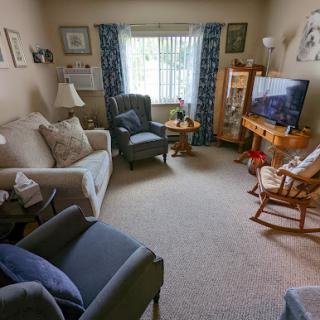 A cozy living room featuring a sofa, chairs, and a television, with natural light filtering through the window.