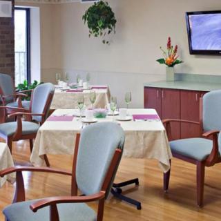 A well-lit dining area featuring neatly arranged tables and chairs, with a television on the wall and indoor plants enhancing the decor.