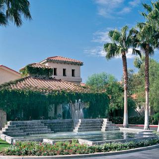 A picturesque building with a vine-covered facade, accompanied by a cascading fountain and palm trees under a clear blue sky.