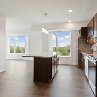 A modern kitchen featuring an island and large windows, with hardwood flooring and ample natural light.