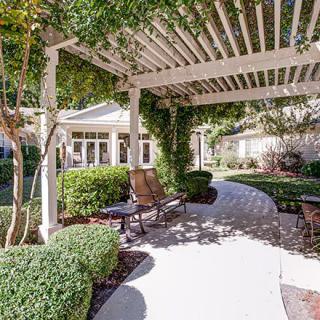 A serene garden pathway with a pergola and outdoor seating.