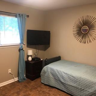 A cozy bedroom featuring a single bed, wall-mounted TV, and decorative wall art.