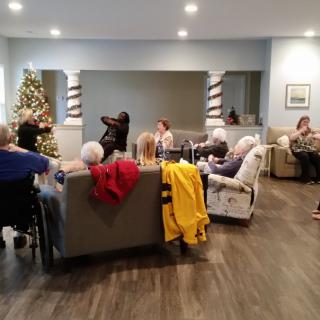 A group of people gathered in a living room with a Christmas tree in the corner.