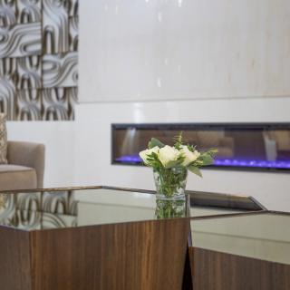 A modern living room with a sleek fireplace, wooden coffee table, and a vase of white flowers.