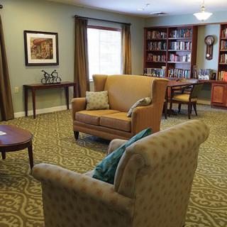 A cozy living room with upholstered chairs, a sofa, bookshelves, and warm lighting.