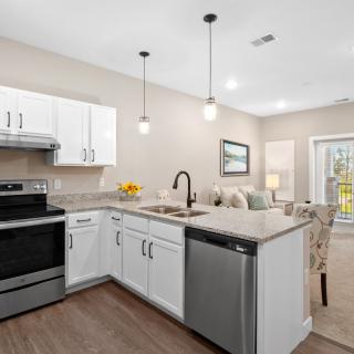 A modern kitchen with white cabinets and stainless steel appliances in an open-concept living space.
