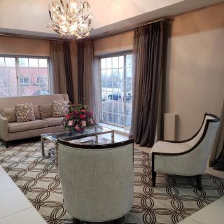 A stylish living room featuring a sofa, armchairs, and a modern chandelier, with large windows and elegant curtains.