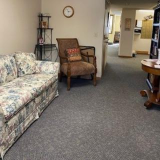 A cozy seating area with a floral sofa and brown chair in a carpeted room.