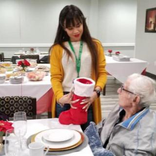 A festive gathering with a young woman presenting a Christmas stocking to an elderly person at a decorated dining table.