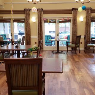 A cozy dining area with wooden tables and chairs, featuring large windows and elegant curtains.