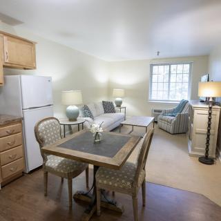 A cozy apartment with a dining area and living room featuring a table, chairs, sofa, and bright lighting.