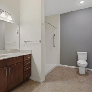 A modern bathroom featuring a toilet, vanity with a sink and mirror, and an enclosed shower area.