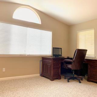 A neatly arranged home office with a wooden desk and leather chair, lit by natural light through the blinds.